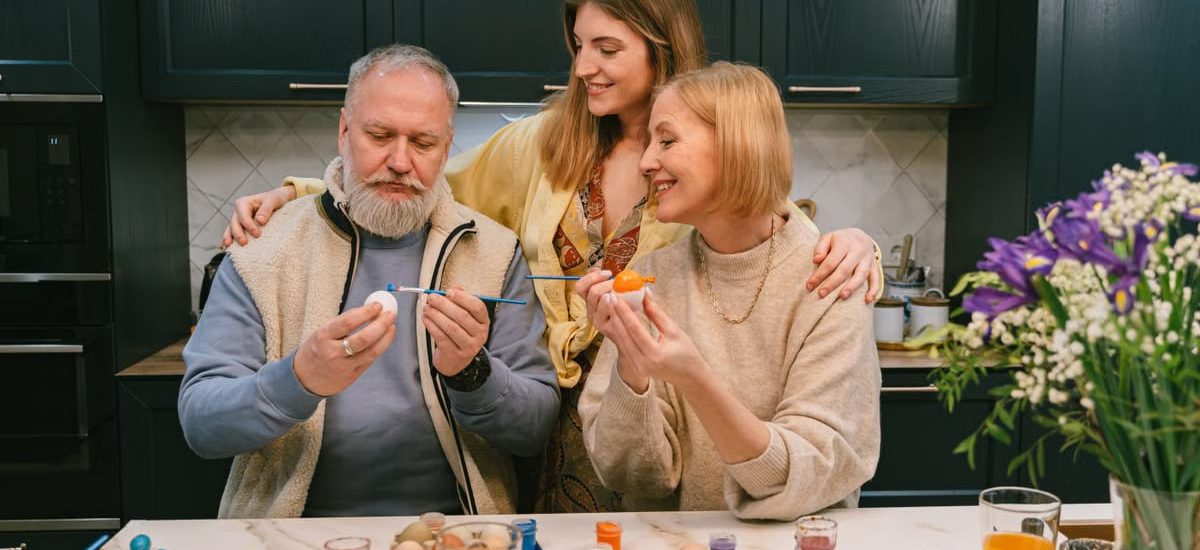 Family gathered in kitchen painting Easter eggs, enjoying a joyful holiday activity.