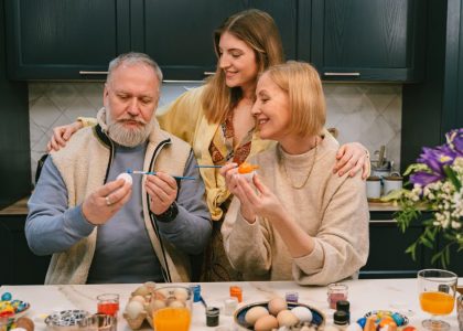 Family gathered in kitchen painting Easter eggs, enjoying a joyful holiday activity.