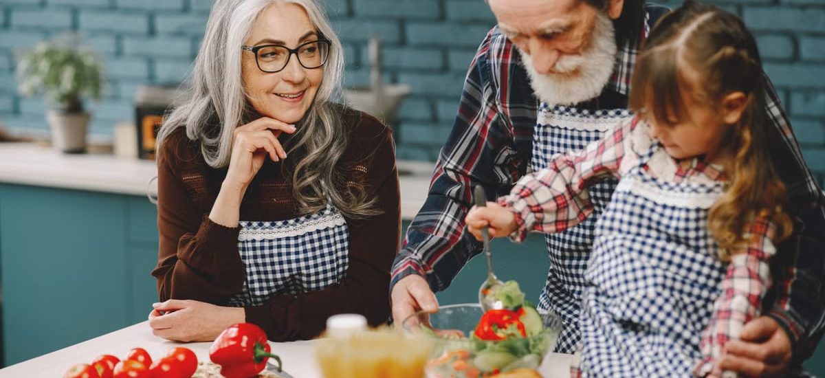 Grandparents and a child enjoy cooking together in a warm kitchen setting.