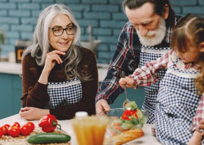 Grandparents and a child enjoy cooking together in a warm kitchen setting.