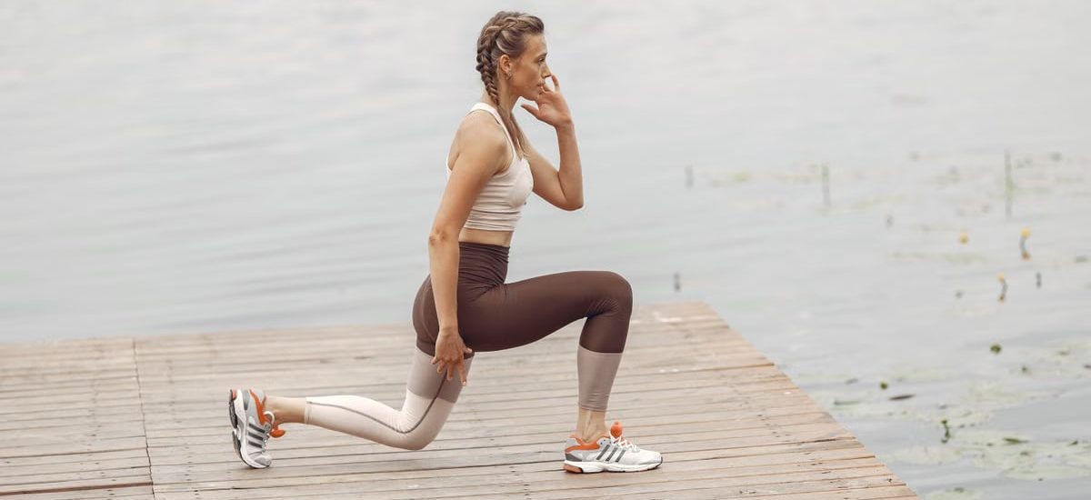 A woman performs lunges on a lakeside wooden deck, showcasing a fit lifestyle outdoors.