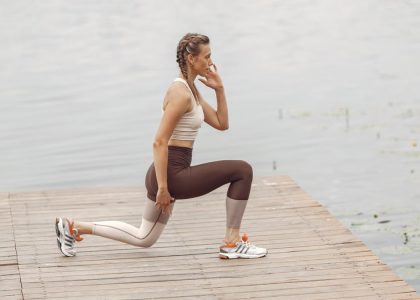 A woman performs lunges on a lakeside wooden deck, showcasing a fit lifestyle outdoors.